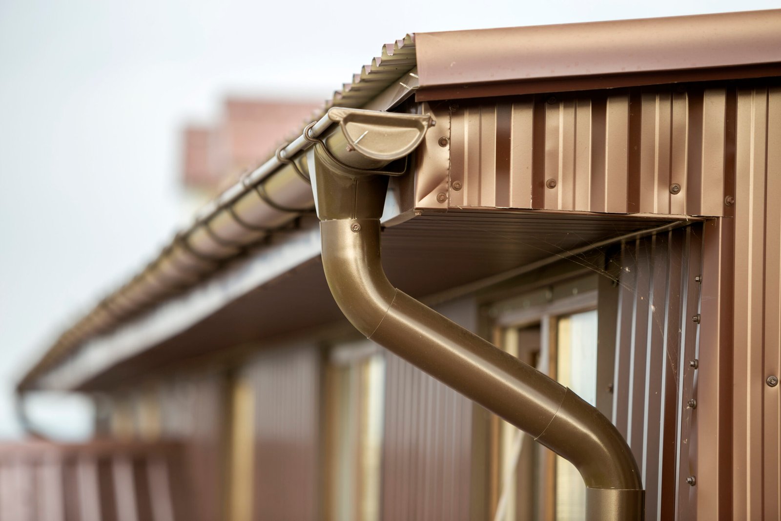 Close-up detail of cottage house corner with metal planks siding and roof with gutter rain system.